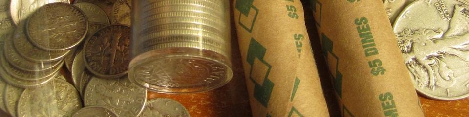 Rolls of dimes and loose silver coins on a wooden surface